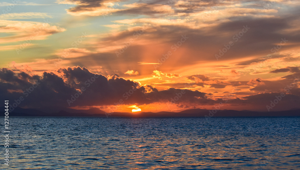 Sunset on the blue sea with clouds. The sun between clouds, .