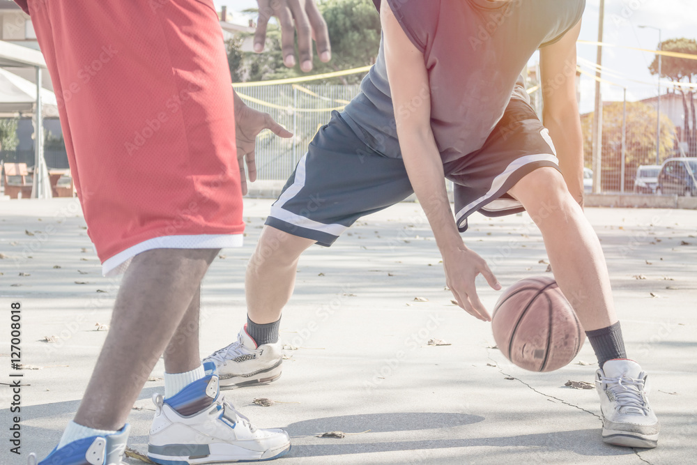 Naklejka premium basketball players in action on a sunny day in open court. close up shot on sport with motion blur on bouncing ball