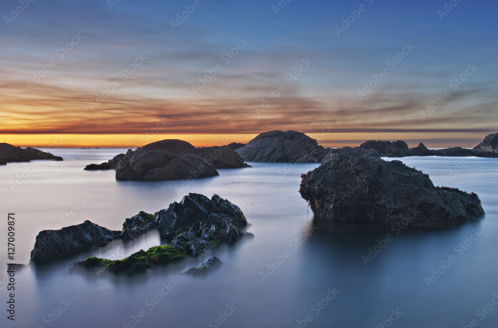 sunset at beach with rocks and blue water