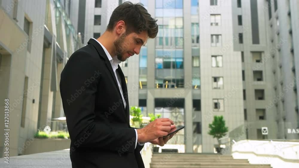 Young serious businessman using tablet and enjoying great summer day out of office. Young serious businessman using tablet and enjoying great summer day out of office.