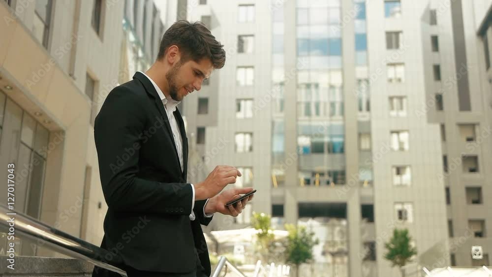Attractive young man wearing stylish suit , using tablet in the street. Attractive young man wearing stylish suit , using tablet in the street.
