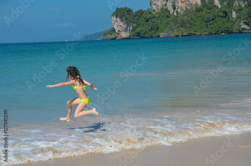 Happy girl plays in sea on tropical beach, child on family vacation 