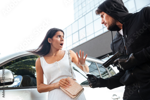 Obraz na plátně Man criminal robbing and threatening with gun to frightened woman