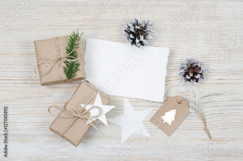 Christmas background. Holiday decorations: gifts, cones, stars on a light wooden table. Paper with space for writing. Top view. © KOSIM