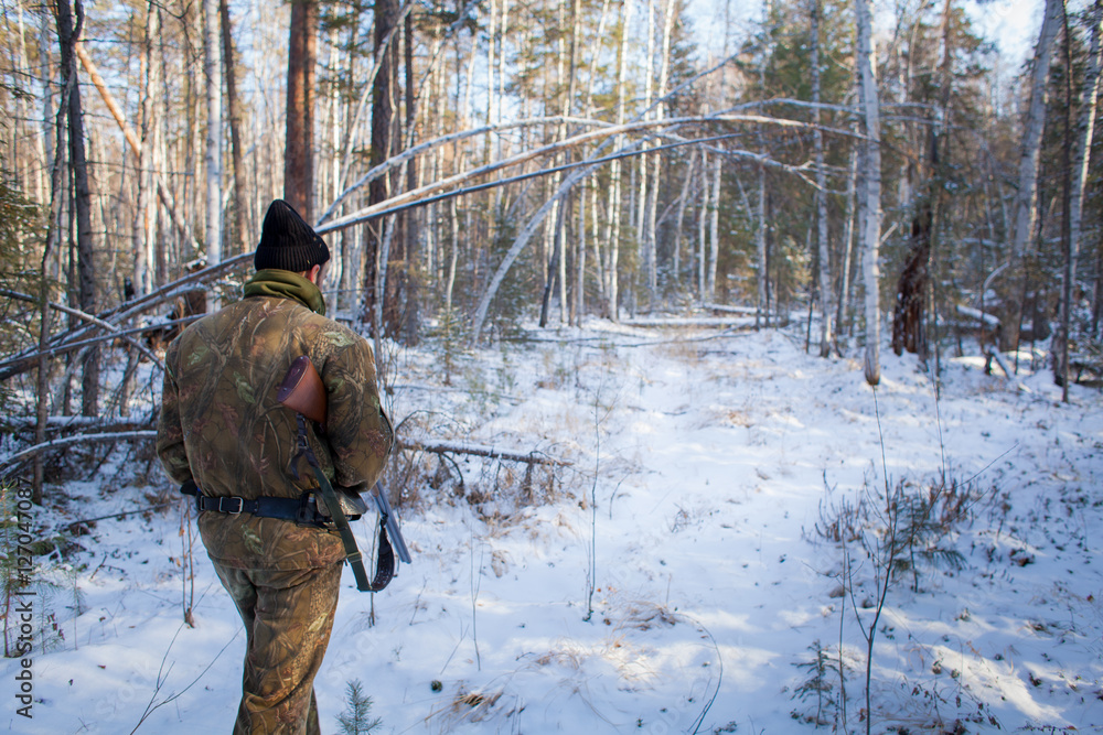Fototapeta premium a hunter in the winter woods with a gun in camouflage clothing.