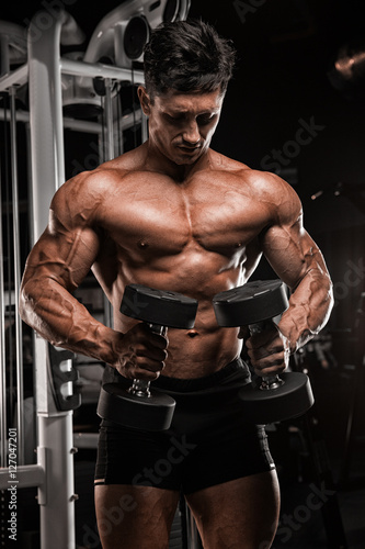 Handsome muscular man with nude body uses his dumbbell to exerci photo