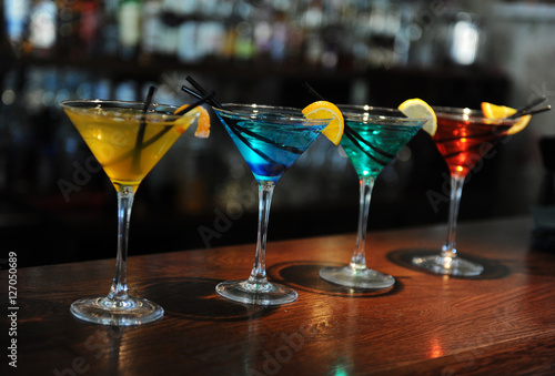 Four colored cocktails on the bar. Yellow, blue, green, red. Decorated with a lemon slice