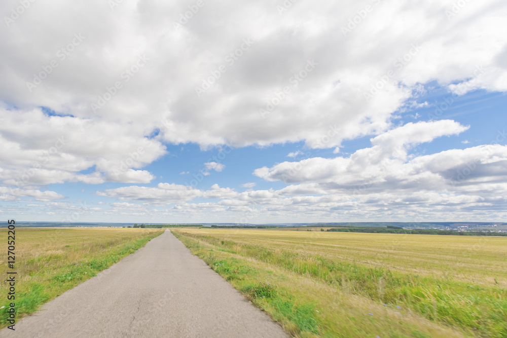 Asphalt road through the field with green grass under blue sky with clouds