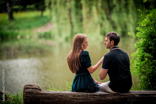 Romance and love. Dating and park. Loving couple sitting together on grass near the lake.