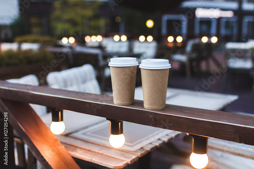 Two cups takeaway coffee on cafe veranda with bokeh lights