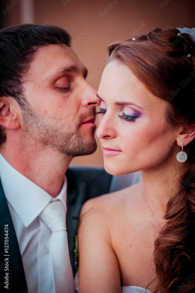 Lovely moment of the newlyweds in the cafe. Bride and groom sitting near large window and kissing each other. Lovely moment of the newlyweds in the cafe. Bride and groom sitting near large window and kissing each other.