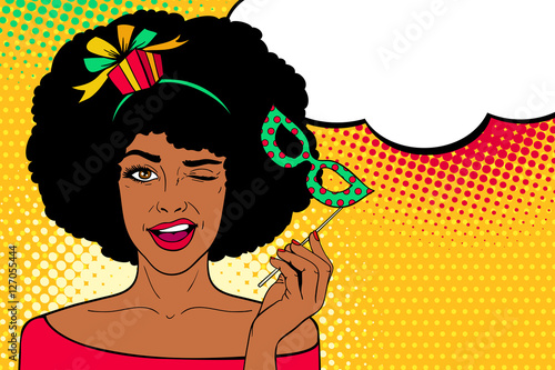 Pop art face. Young sexy afro american woman with gift on her head and carnival mask in her hand smiles and winks with speech bubble. Vector illustration in retro comic style. Party invitation.
