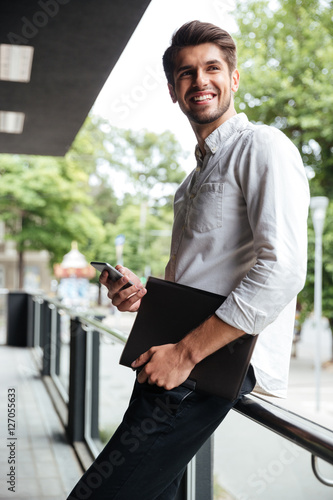 Businessman holding folder and using mobile phone outdoors
