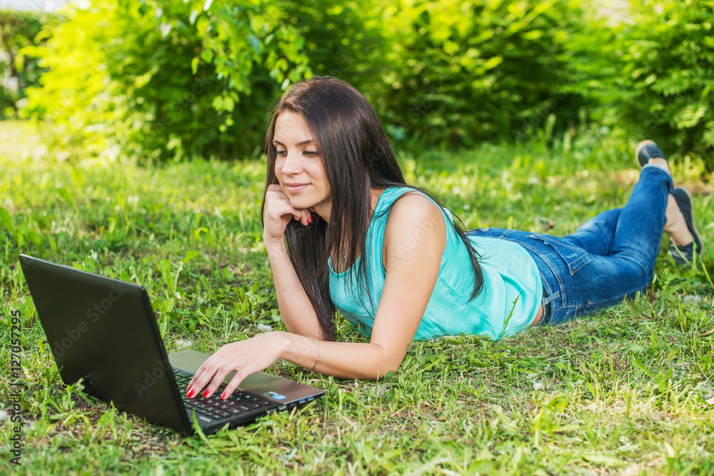 Young woman lying on the grass, using laptop and typing Young woman lying on the grass, using laptop and typing