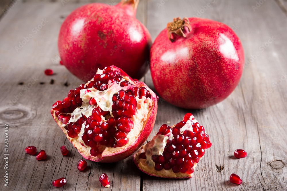 Whole and broken red ripe juicy pomegranates on rustic wooden unpainted table Whole and broken red ripe juicy pomegranates on rustic wooden unpainted table