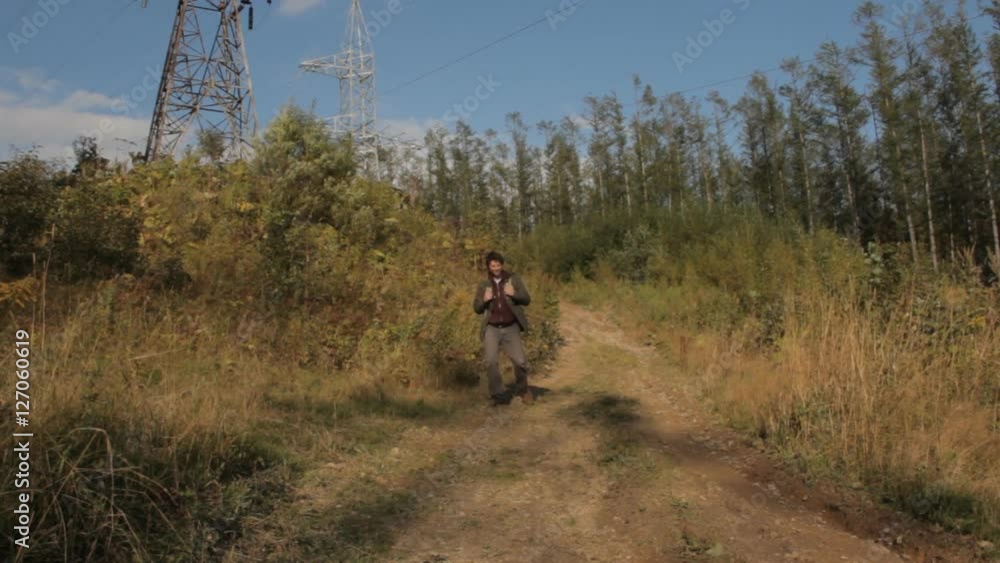 A middle aged man with a beard with a backpack walking down a mountain path. He stops, puts a hand to the forehead protecting from the bright sun, looks into the distance and walks on. A middle aged man with a beard with a backpack walking down a mountain path. He stops, puts a hand to the forehead protecting from the bright sun, looks into the distance and walks on.