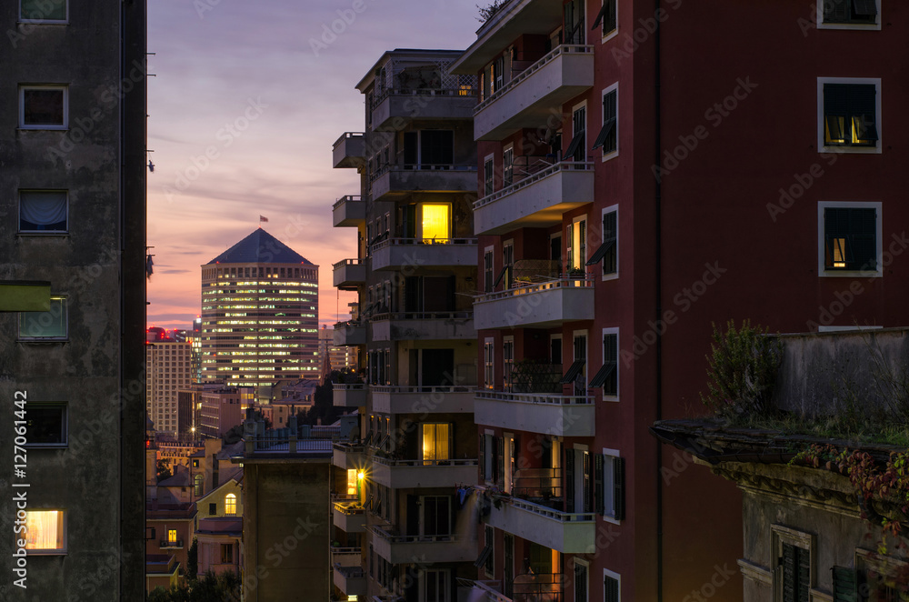 Fototapeta premium View from the inside of the residential neighborhood of Genoa, San Teodoro, to the famous skyscraper San Benigno North Tower, also known as Matitone, all lit up in this beautiful urban evening.
