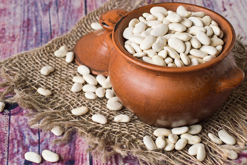 Beans.   Clay pot with white beans on sackcloth on an old wooden table.