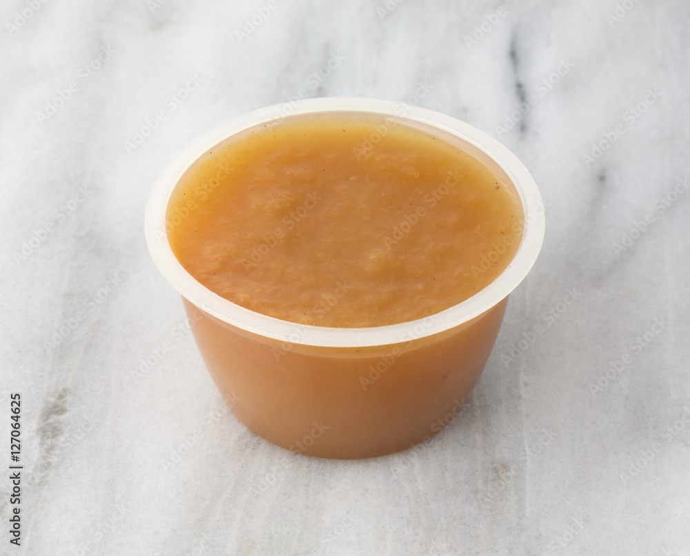 Cinnamon applesauce in a plastic container on a marble table top. Cinnamon applesauce in a plastic container on a marble table top.