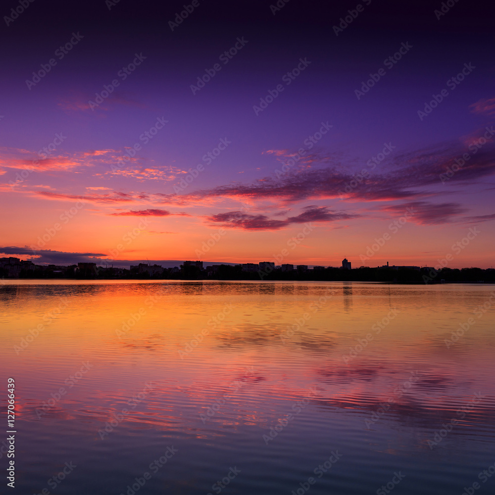 Obraz premium fantastic sunrise over lake. wonderful morning scene. colorful sky reflected in the water. the silhouette city on the horizon. calm morning lake, beautiful view. use as background. square