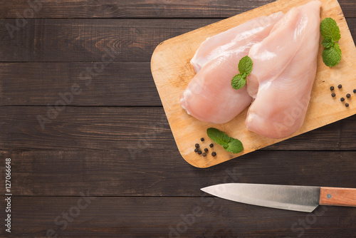 Top view raw chicken on cutting board and knife on wooden background.