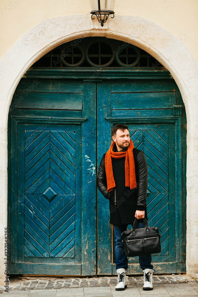 handsome and young man in a black coat standing near green doors