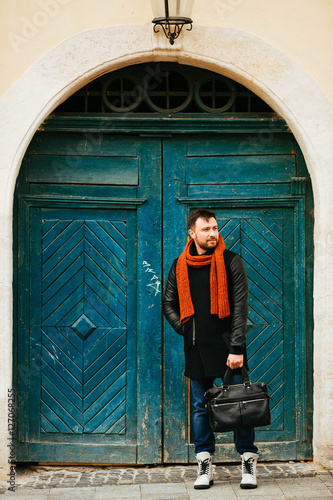 handsome and young man in a black coat standing near green doors photo