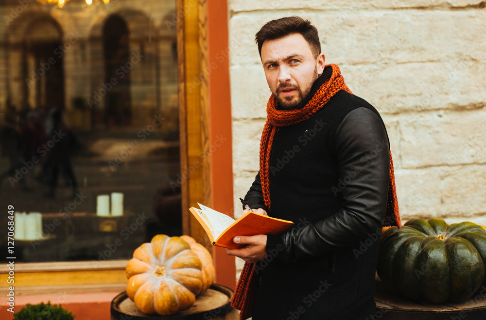 handsome and young man in a black coat reading a book outdoors