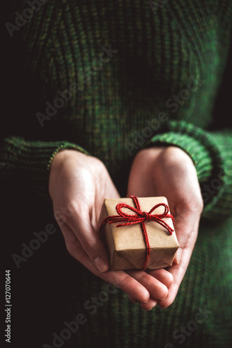 Hands holding small gift with red bow. Hands folded in heart shape holding small present for birthday, Christmas, Valentines day, Thanksgiving Day; Mothers day. Close up.
