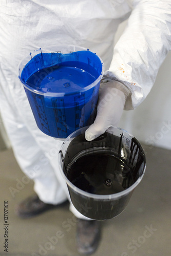 The Netherlands, Utrecht. Inside the factory of a Dutch design furniture brand.  A painter holding two buckets of paint. One blue and one black. photo