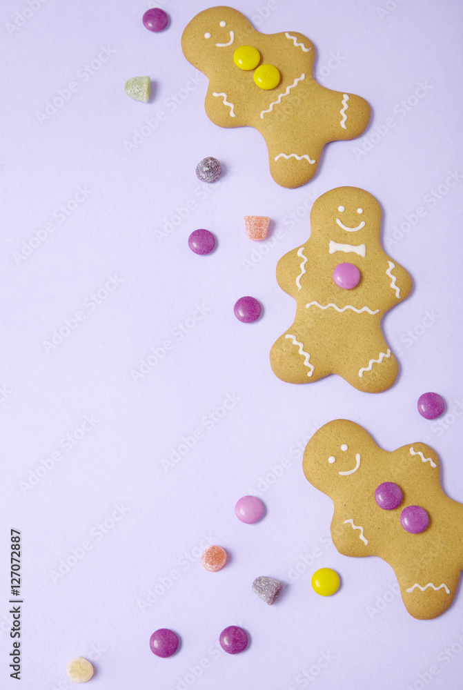 Hand decorated gingerbread men on a pastel purple background with sweets and blank space at side Hand decorated gingerbread men on a pastel purple background with sweets and blank space at side