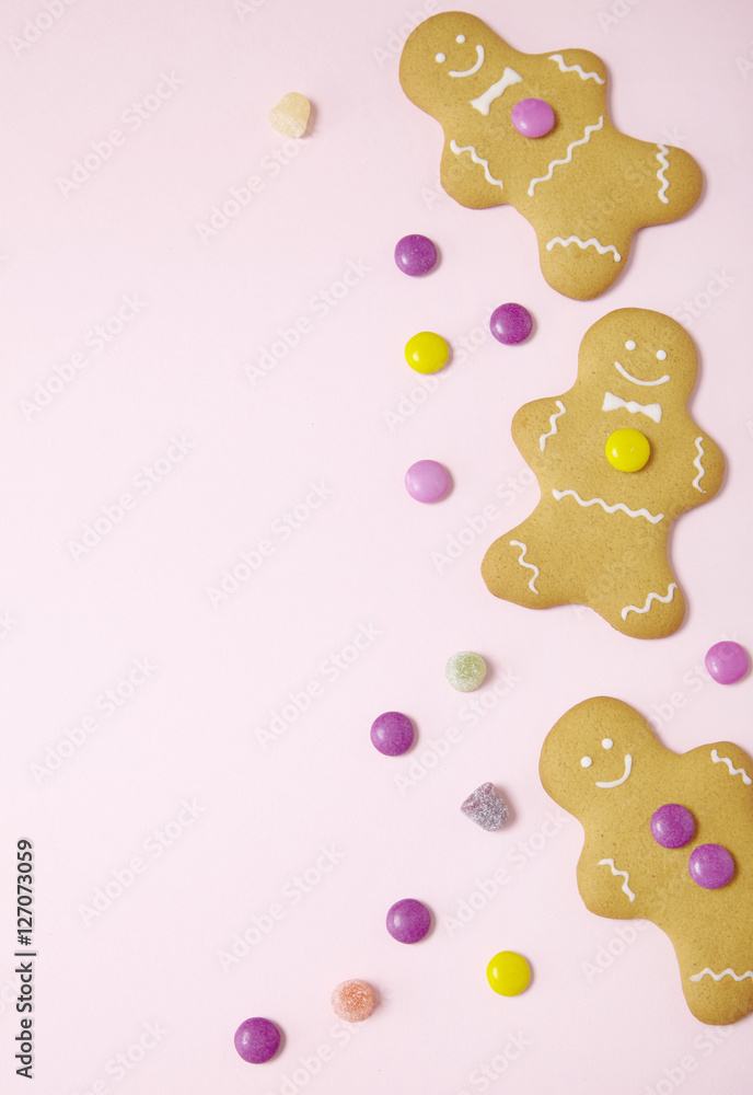 Naklejka premium Hand decorated gingerbread men on a pastel pink background with sweets arranged to form a page frame