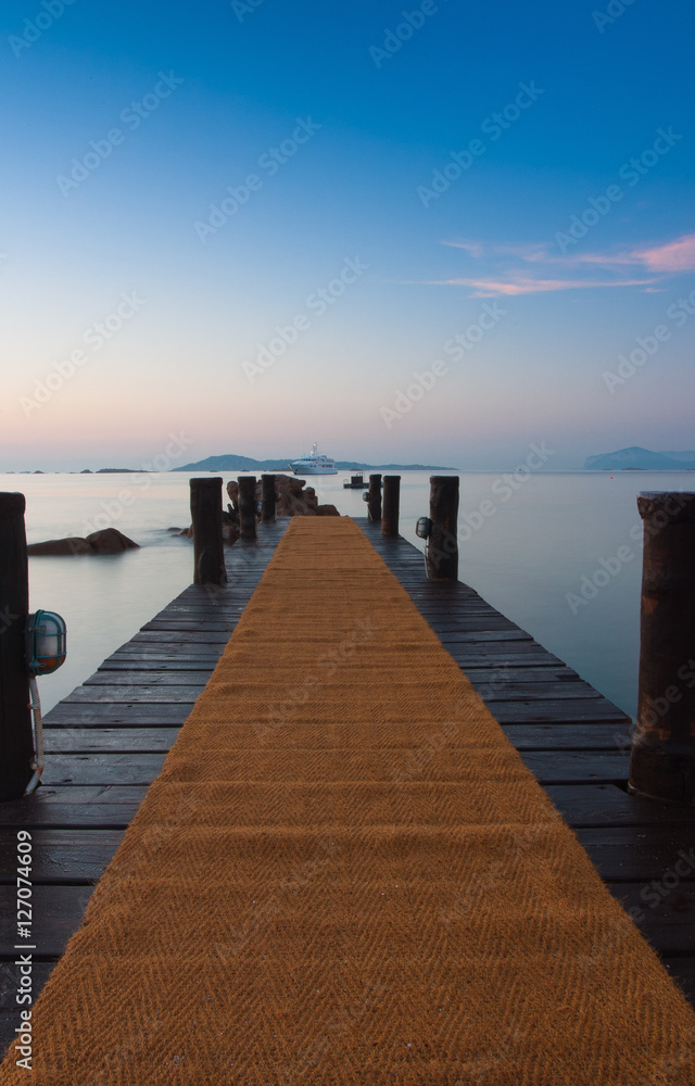 Fototapeta premium Wschód słońca na plaży. Drewniane molo w Romazzino, Sardynia, Włochy