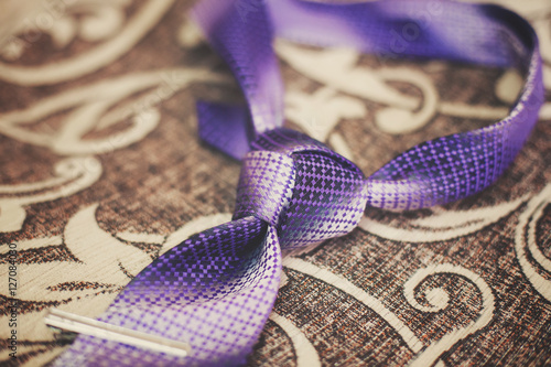 Purple necktie with trinity tie knot on sofa, vintage toned