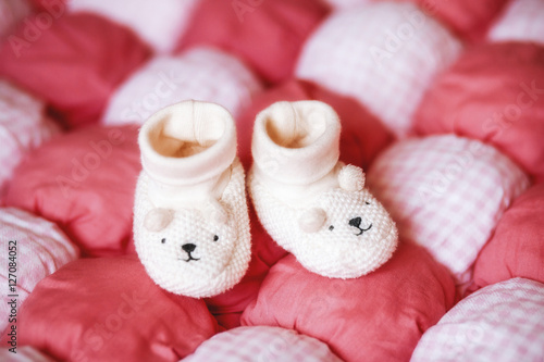 Cute white baby booties on red blanket. Pregnancy concept