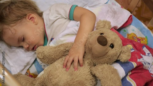 the sweet baby sleeps in a cot with a teddy bear