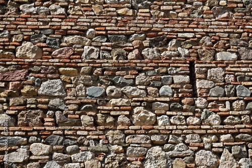 Detail of a horizontal stony wall made of thin and thick rows of bricks and stones
