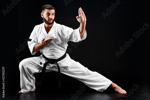 Karate man in a kimono in fighting stance on a black background