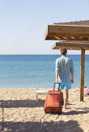 Man in sunglasses with luggage on the sea in summer sunny day