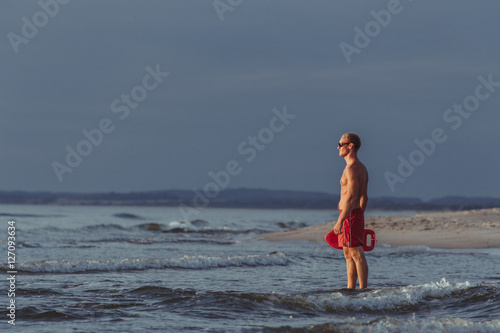lifeguard on the beach with glasses, with a life buoy, wet sand and sea at sunset