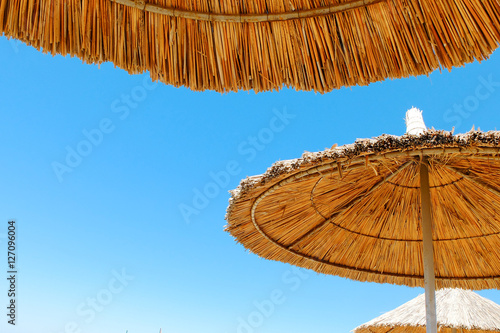 Three beach umbrellas made of straw at blue sky background