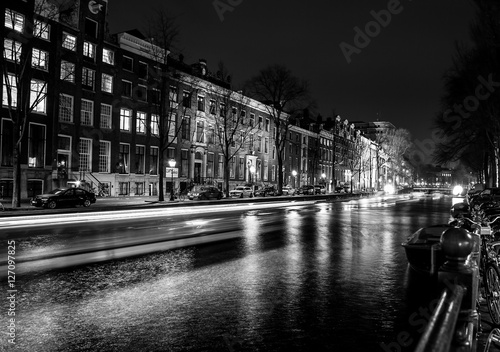 AMSTERDAM, NETHERLANDS - DECEMBER 14, 2015: Black-white photo of cruise boat moving on night canals of Amsterdam in Amsterdam, Netherlands. photo