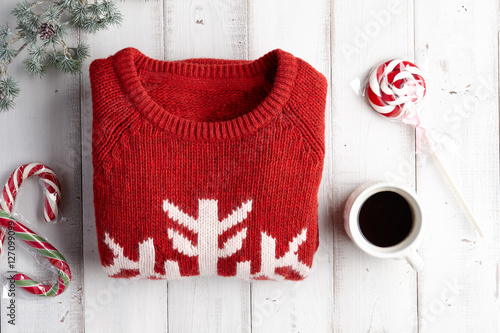 Winter holiday knitted sweater, hot coffee and lollipops on white wooden background