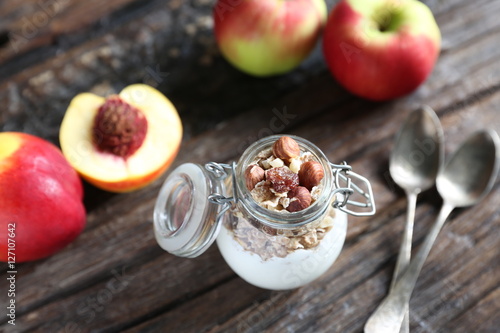 Glass jar with yogurt, granolla and almond nuts in it. Nectarin and apples are on the wooden backgound with spoons closed to the jar. photo