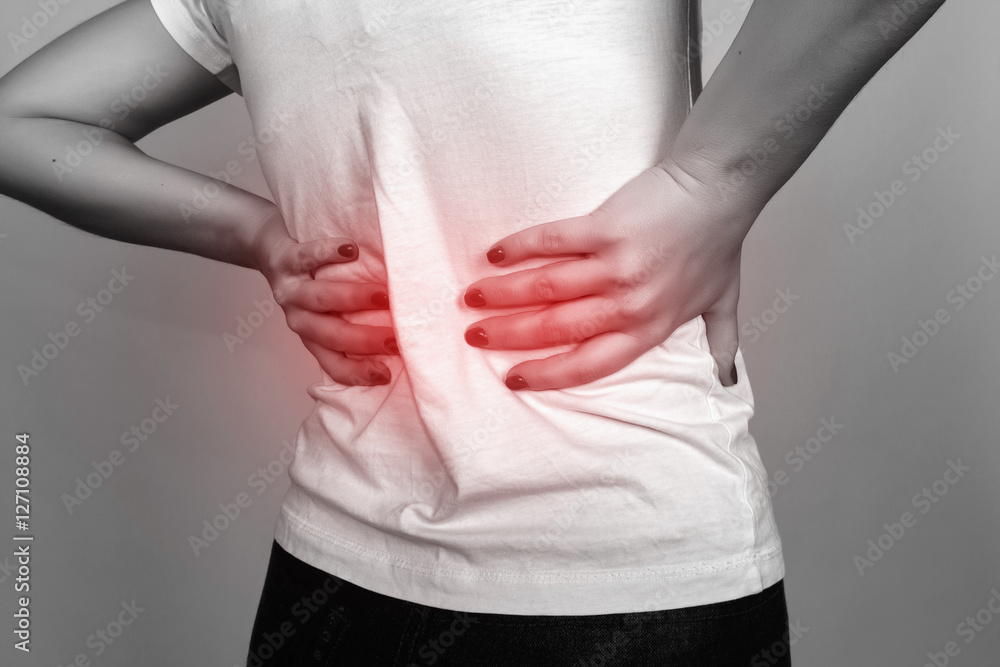 Closeup portrait of a pretty woman suffers from backache standing over gray background black and white with red accent Closeup portrait of a pretty woman suffers from backache standing over gray background black and white with red accent