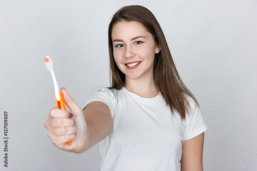 Beautiful young woman gives a toothbrush standing over gray background Beautiful young woman gives a toothbrush standing over gray background