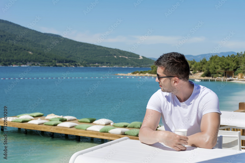 young handsome man drinking coffee on the beach.Summer leisure 