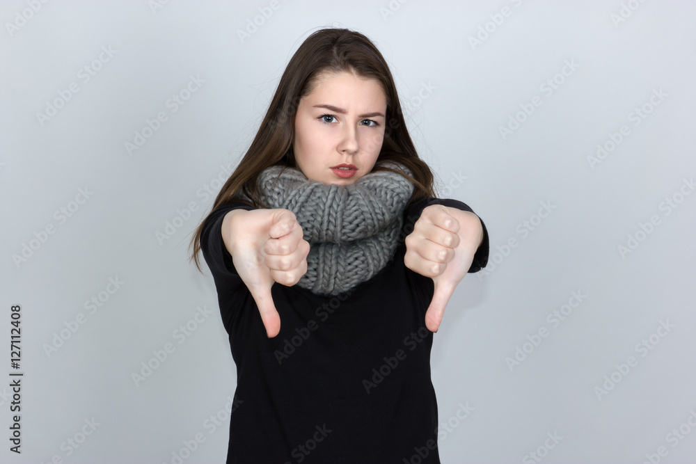 Portrait of a pretty woman in turtleneck sweater with scarf showing thumbs down standing over gray background and looking at camera. Portrait of a pretty woman in turtleneck sweater with scarf showing thumbs down standing over gray background and looking at camera.