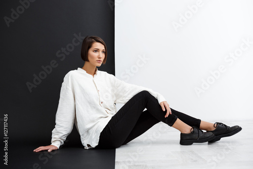Young beautiful girl sitting on floor over black and white background.