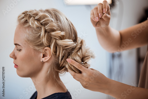 Female hairdresser making hairstyle to blonde girl in beauty salon. photo